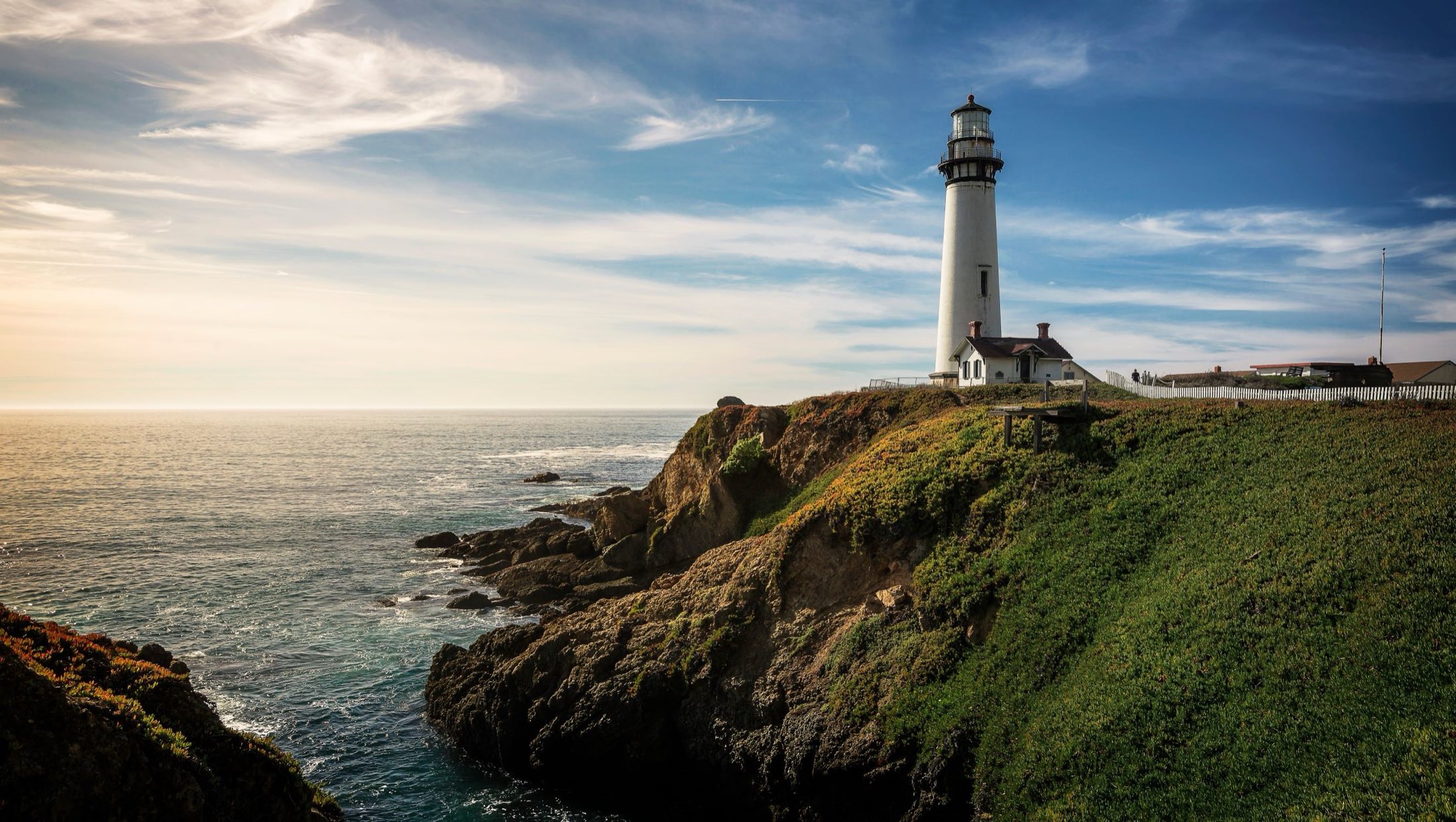 A white lighthouse on a rocky stretch of coastline at dusk
